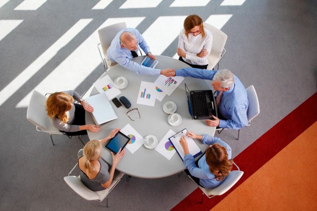 A team of five collaborating around a table with documents and laptops.