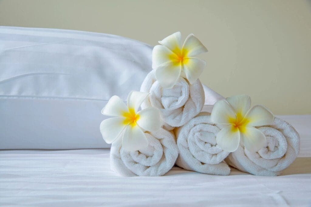 Rolled white towels decorated with yellow and white flowers on a bed.