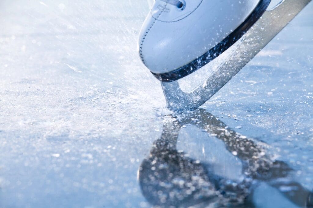 Close-up of an ice skate blade gliding on ice, creating ice shavings.