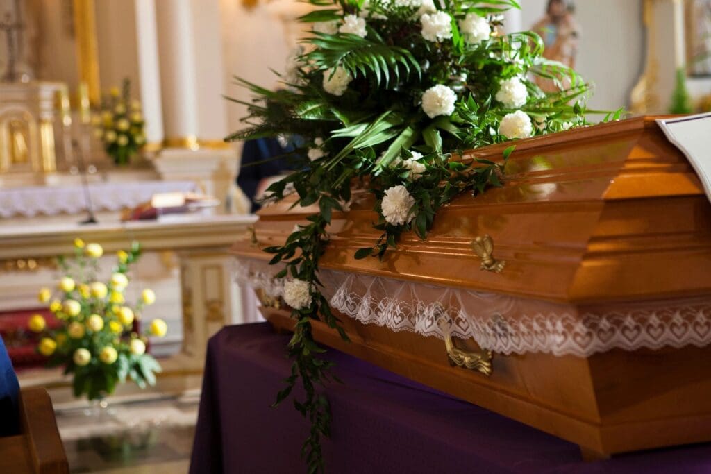 A flower-adorned wooden coffin in a solemn funeral setting.