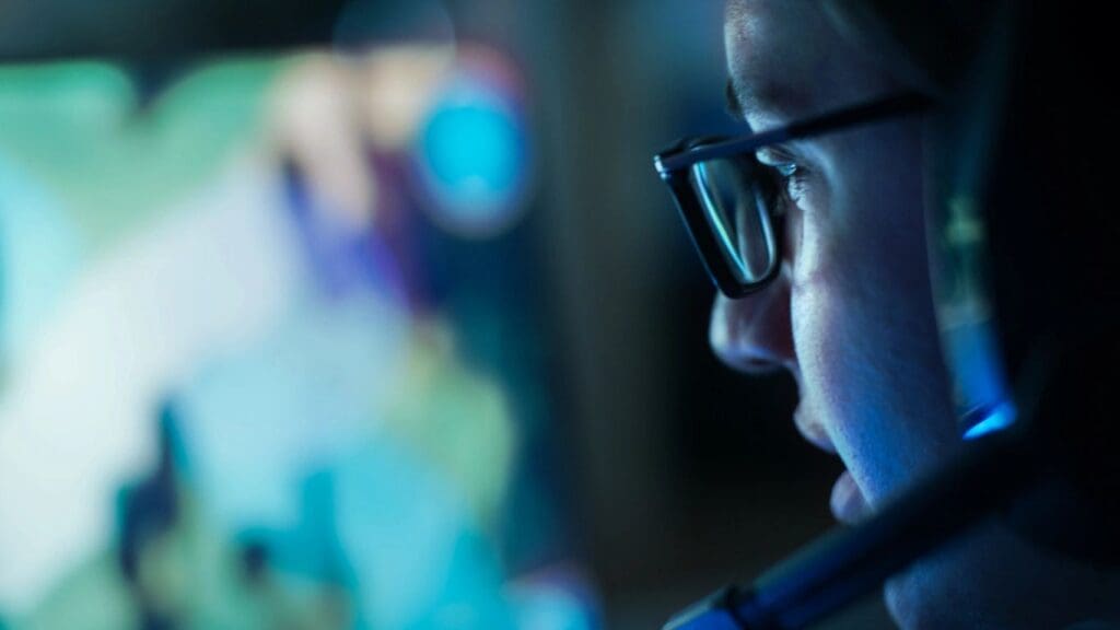 Person wearing glasses focused on a screen with a blurred background.