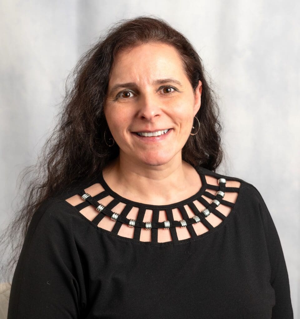 Smiling woman with long curly hair wearing a black top with a decorative neckline.