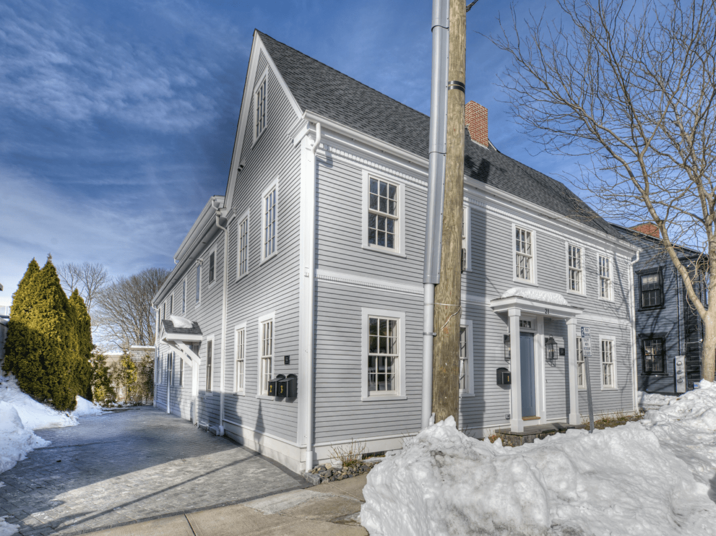 A large gray house with white trim on a snowy day under a clear blue sky.