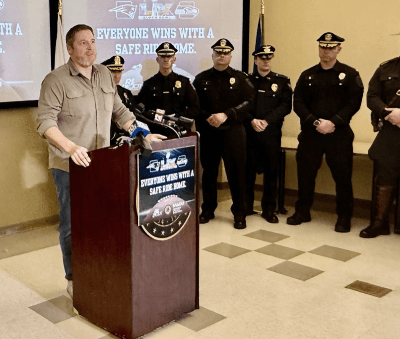Police officers and a man stand at a podium during a public safety event.