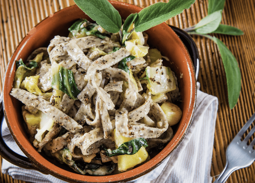 A bowl of creamy pasta with fresh herbs and zucchini.
