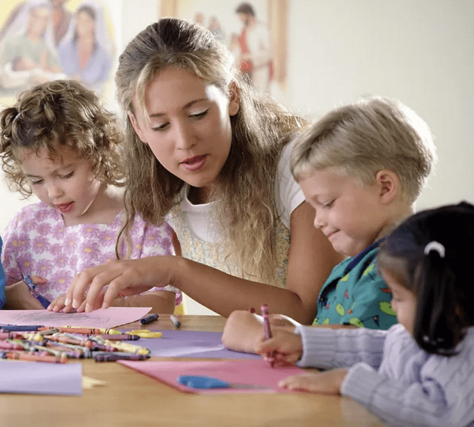 A woman helping children with crafts at a table.