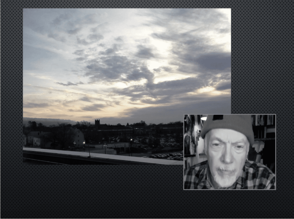 Sunset with cloudy sky over a cityscape, video call window with a man's face.