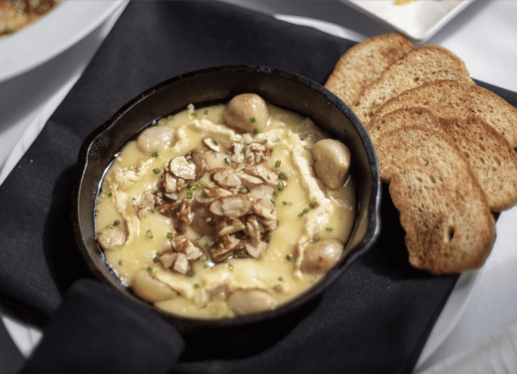 Baked cheese dip topped with nuts served with toasted bread slices.