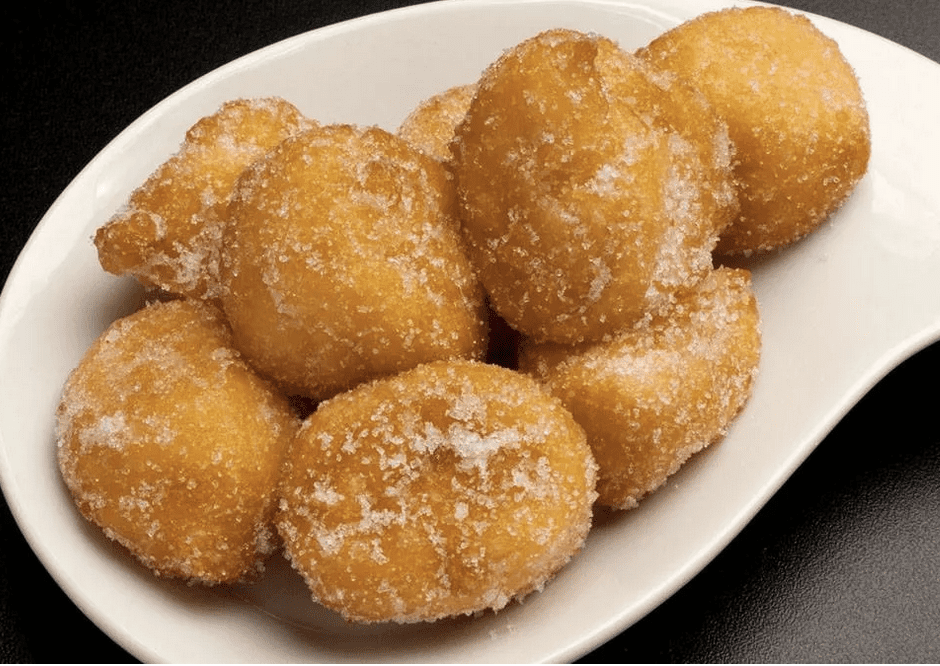 Sugary fried doughnuts piled on a white plate.