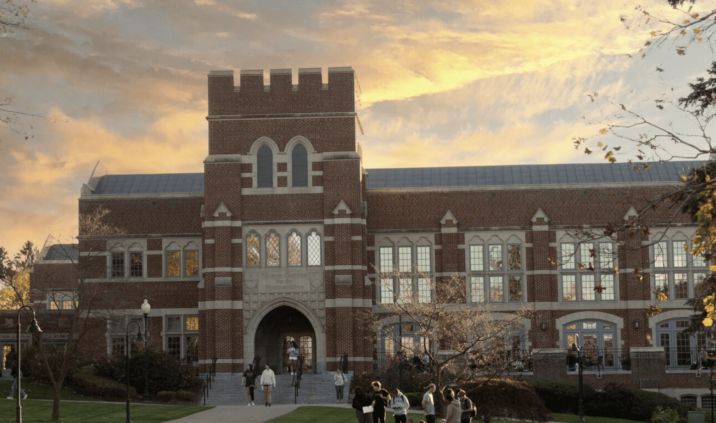 Historic brick university building at sunset with people gathered outside.