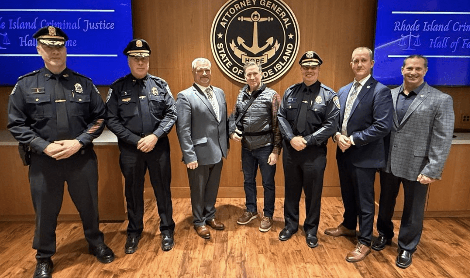 Group photo of two police officers and three men in formal attire inside a room with a seal.