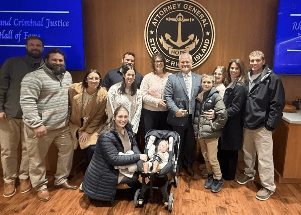 Group photo of diverse people smiling in front of a seal, with a baby stroller in the center.