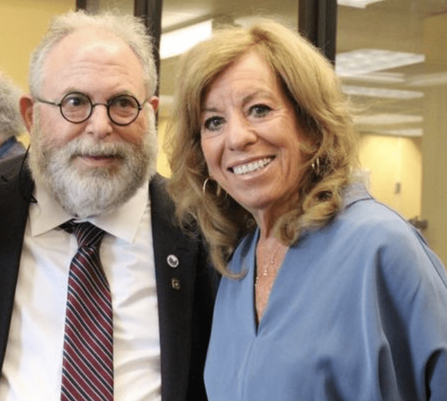 Two smiling adults posing indoors, dressed in business attire.