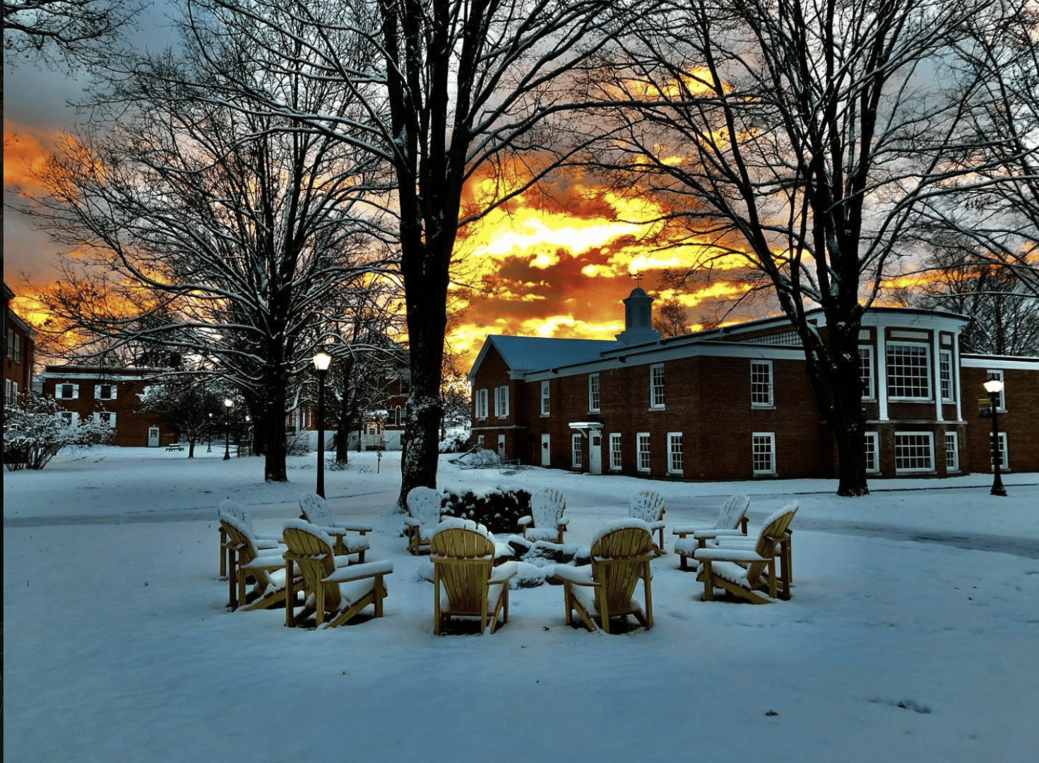 Snow-covered courtyard with fire pit chairs at sunset.