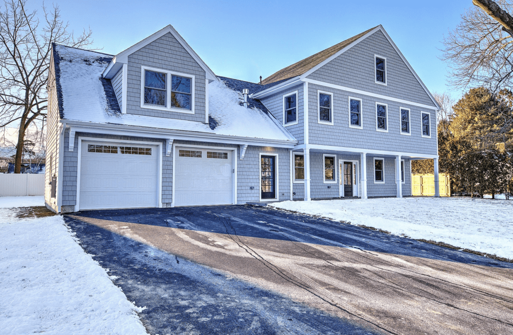 Modern gray house with snow-covered roof and driveway.