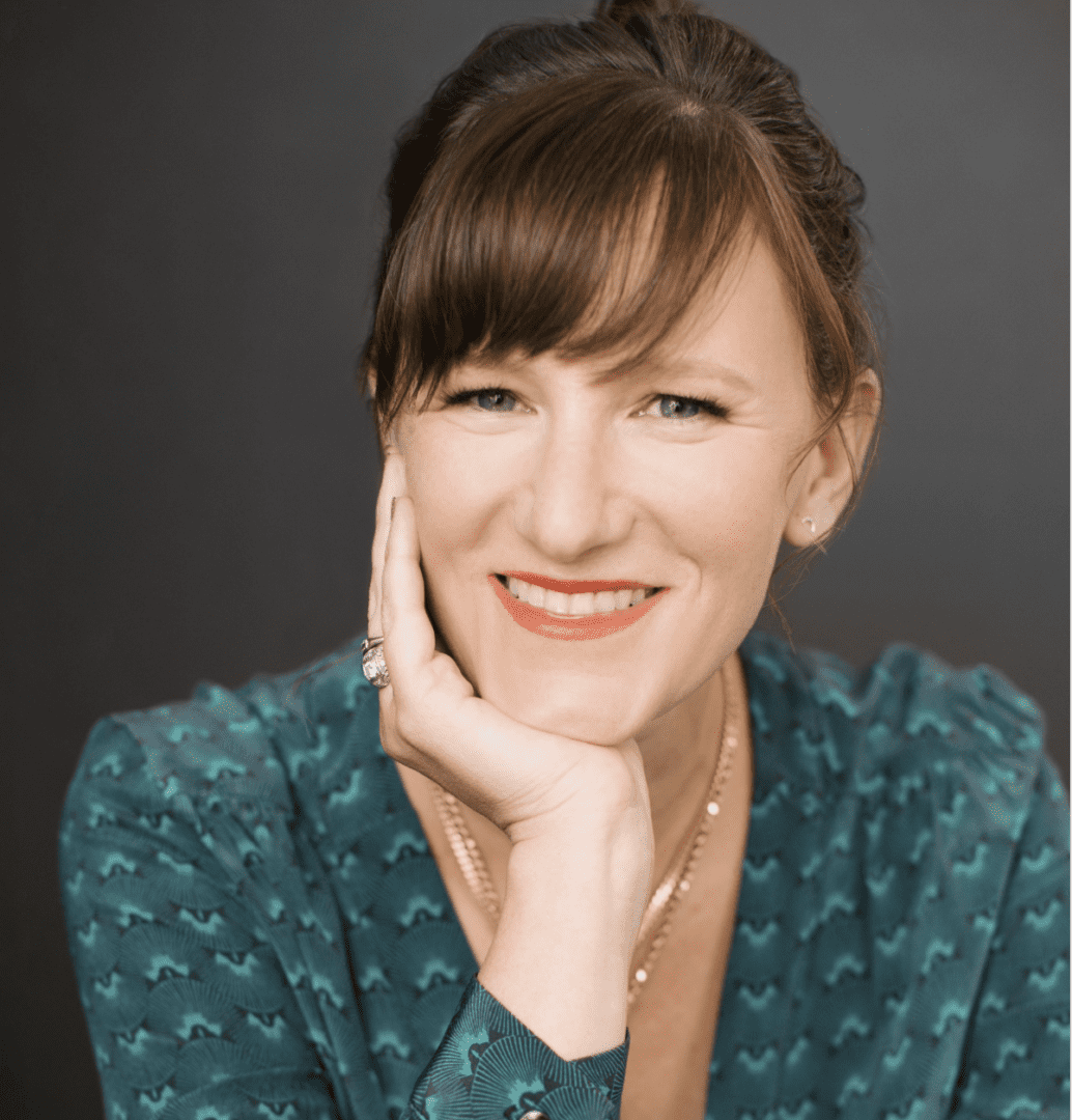 Smiling woman resting her chin on her hand, wearing a teal patterned shirt.