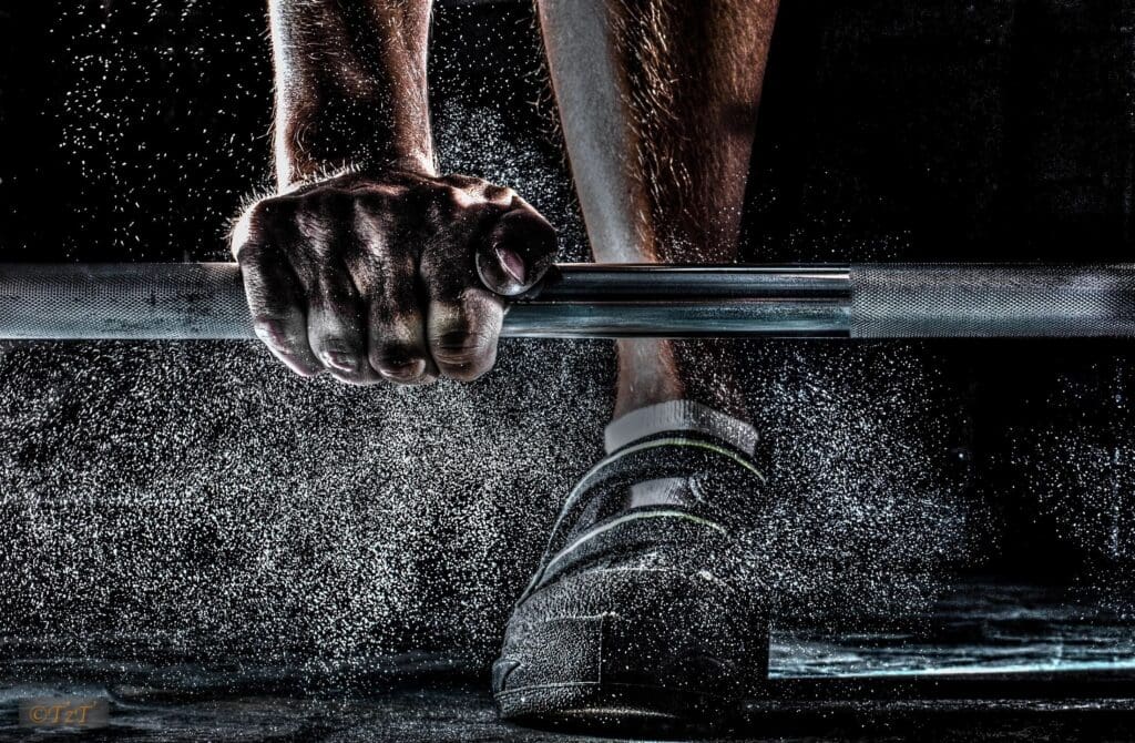 Close-up of hands gripping a barbell with chalk dust in the air.