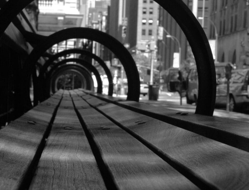 Black and white image of a wooden bench with circular metal arches in an urban setting.