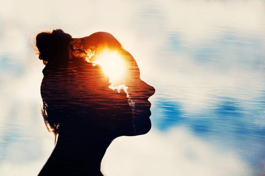 Silhouette of a woman with the sun shining through her head against a cloudy sky.