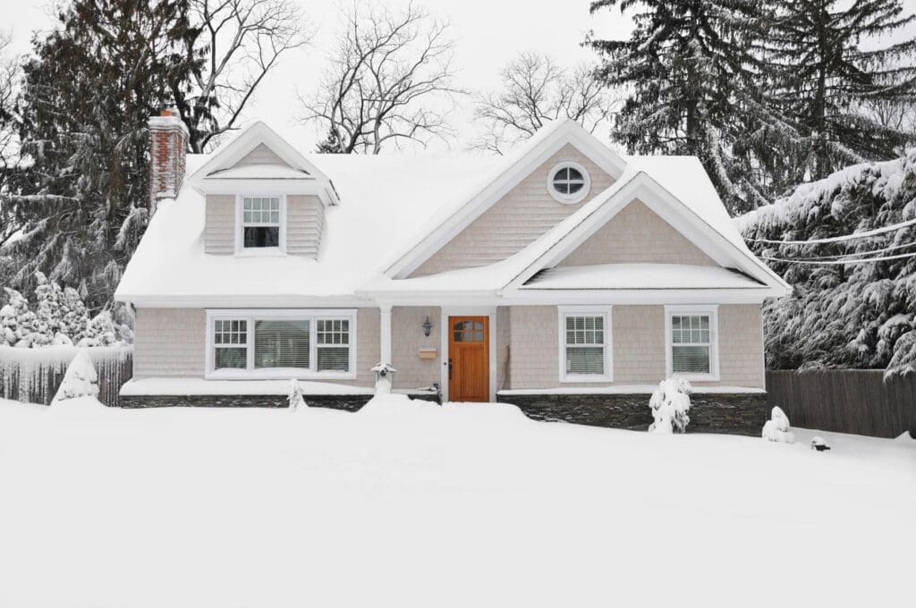 A snow-covered house with a wooden front door and surrounding trees.