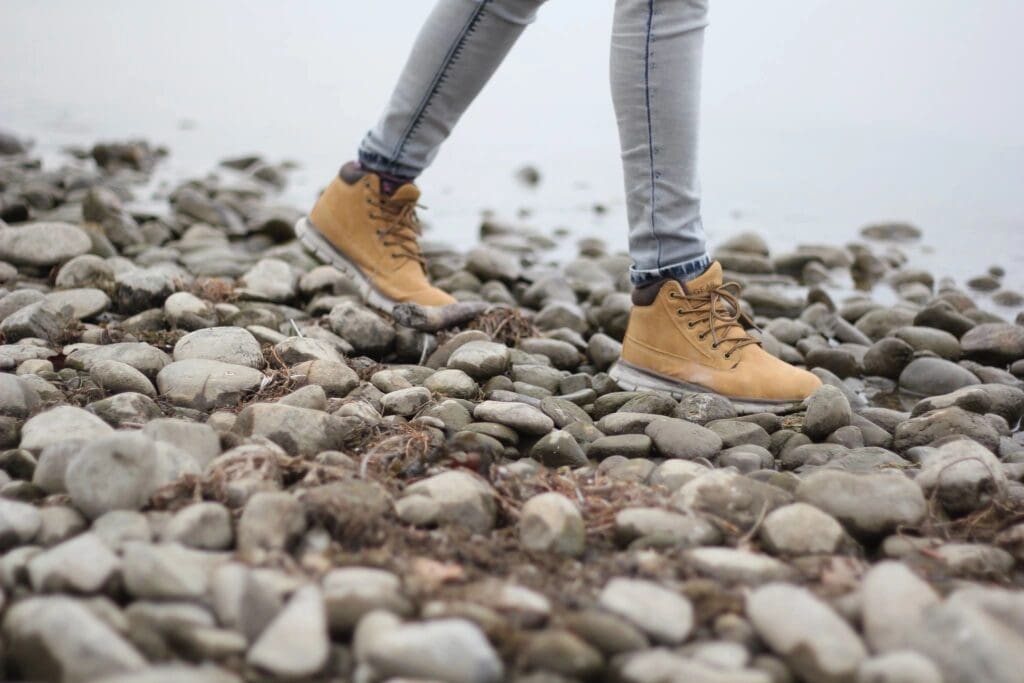Person walking on rocky terrain wearing yellow boots and gray pants.