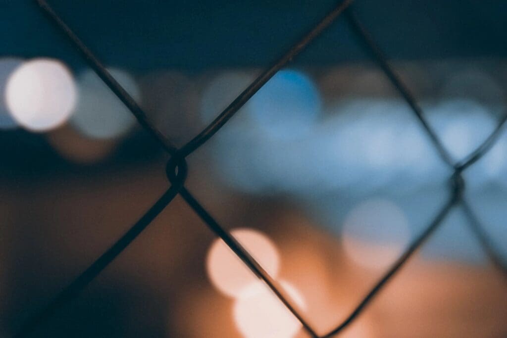 Close-up of a chain-link fence with blurry lights in the background.