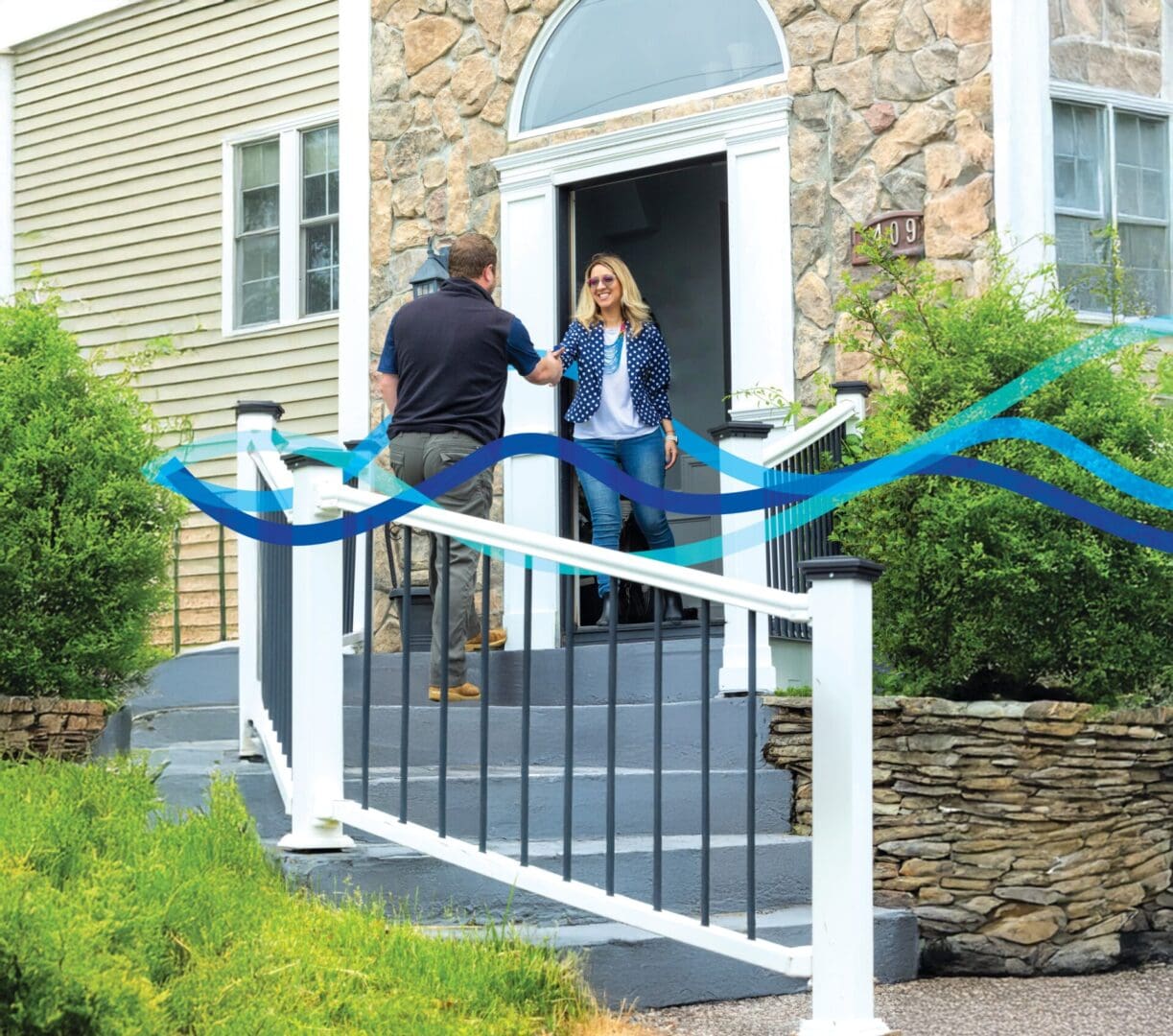 A couple standing outside a house entrance with a white fence in front.