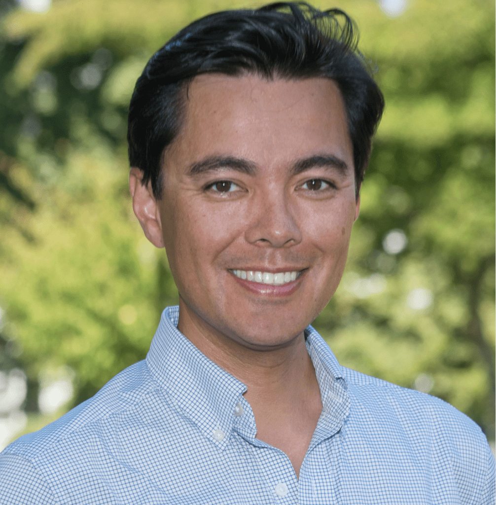 Smiling man outdoors in a light blue shirt.