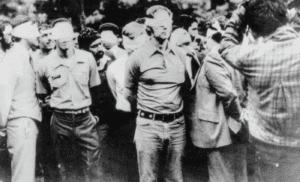 Black and white photo of men in civilian clothes standing with hands behind their backs.