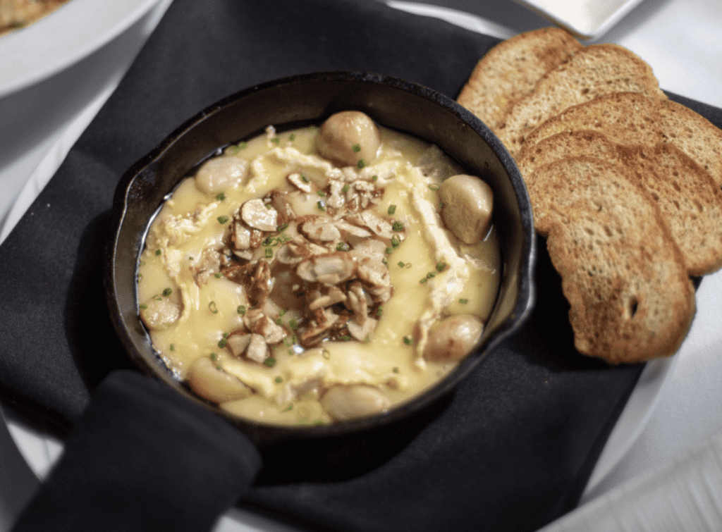 Baked Brie topped with roasted garlic, glazed almonds, and spiced honey served with crostini