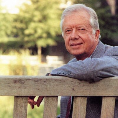 A man leaning on a wooden bench in the park.