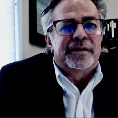 A man in glasses is sitting in front of a desk.