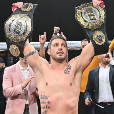 Gary Balletto, a man with tattoos, holding up his belts in front of a crowd.