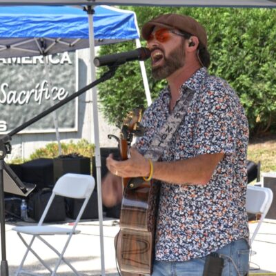 Man singing and playing guitar outdoors under a blue canopy.
