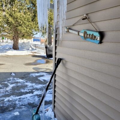 A shovel with icicles hanging from the side of a house.