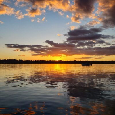 The sun is setting over a lake with a boat in the water.