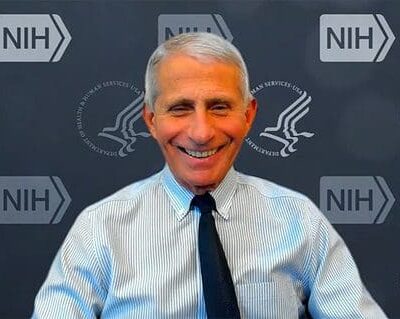 An older man smiling in front of a nhs logo.