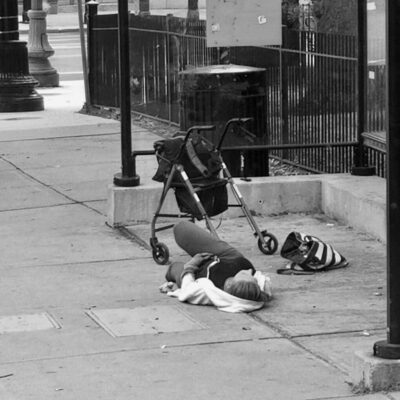 A person is laying on the sidewalk with a stroller.