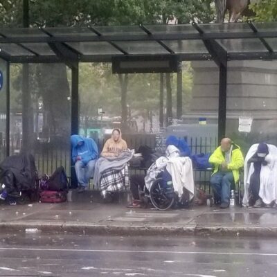 A group of people sitting at a bus stop in the rain.