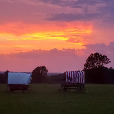 Covered wagons at sunset, American flag.