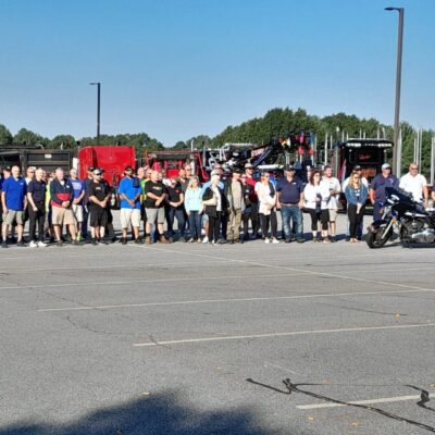 Large group of people standing by trucks and motorcycle.