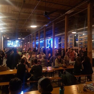 A crowd of people sitting at tables in a large warehouse.