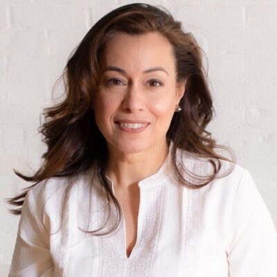 A woman in a white shirt smiling in front of a community preparatory school.