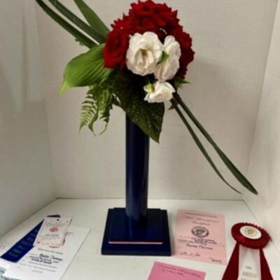 A vase with roses, flowers, and ribbons on it.