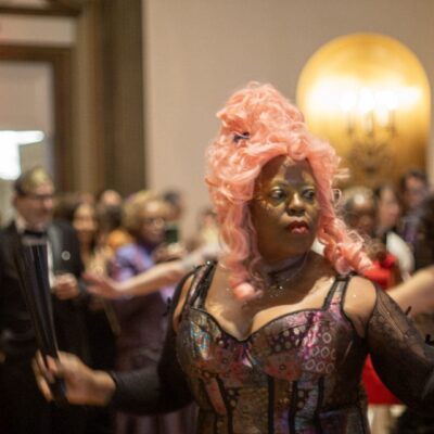 Person in elaborate costume and pink wig at a crowded event.
