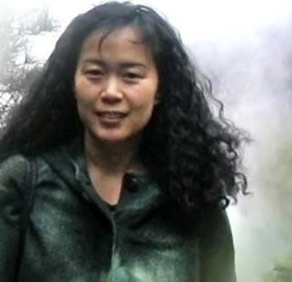 Woman with curly hair smiling outdoors in a misty environment.