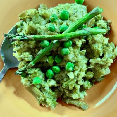 Risotto with asparagus and peas on an orange plate.