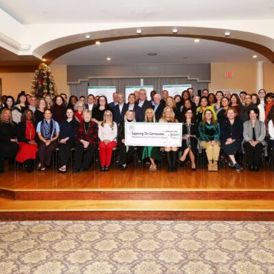 Large group posing with a giant check in a festive indoor setting.