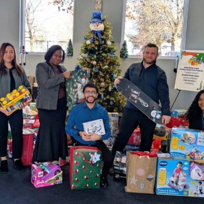Group of four people posing with wrapped holiday gifts and a decorated Christmas tree indoors.