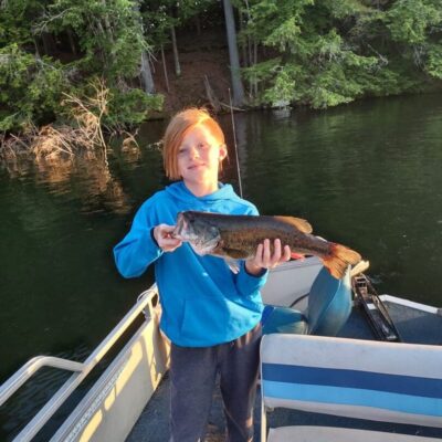 A young girl holding up a fish on a boat.